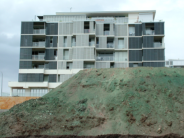 A large pile of dirt is sitting in front of a residential apartment building.