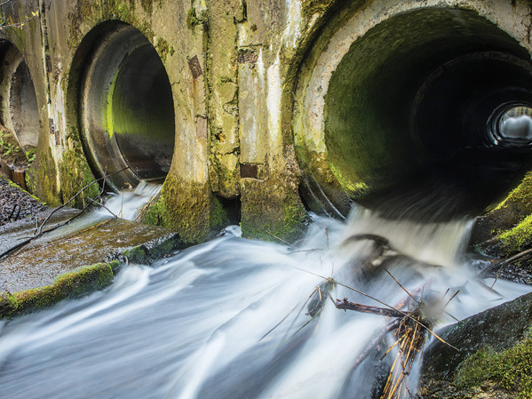 Water flowing through concrete pipes covered in moss